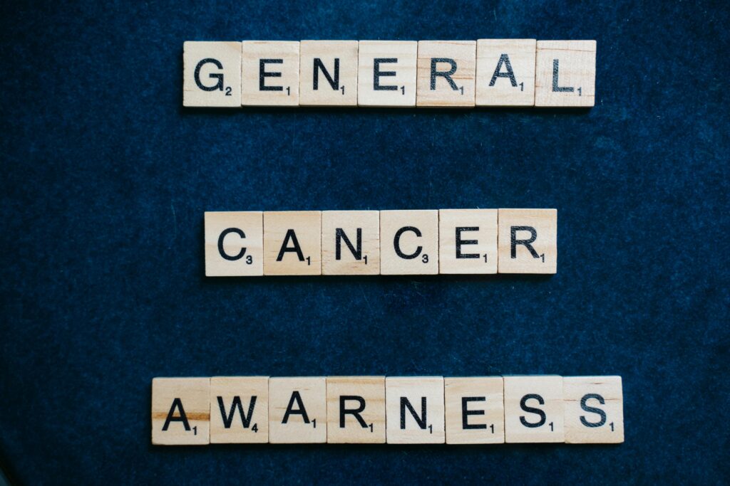 Words 'General Cancer Awareness' spelled with Scrabble tiles on a blue surface, promoting awareness.